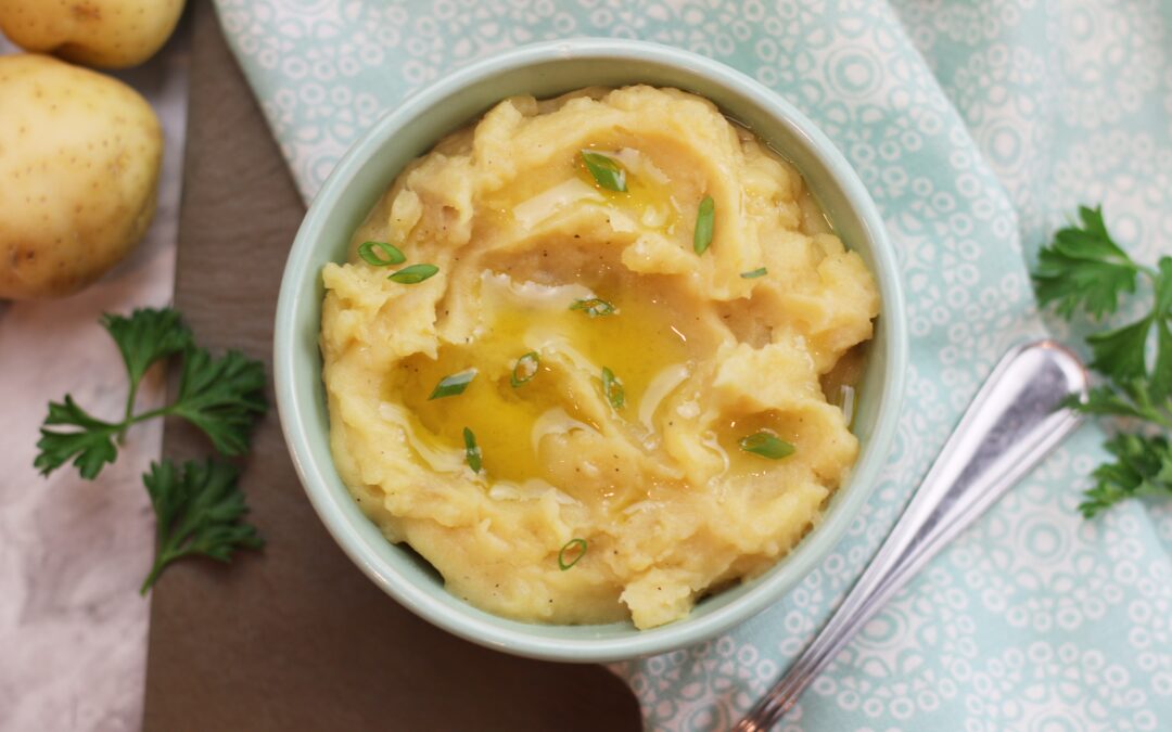 A bowl of mashed potatoes garnished with green onions and a drizzle of olive oil