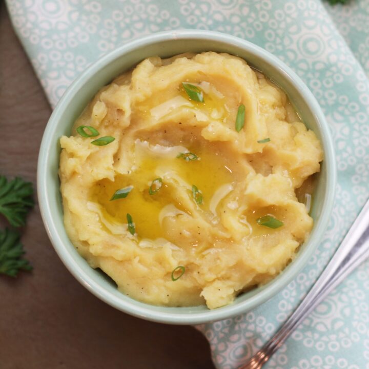 A bowl of mashed potatoes garnished with green onions and a drizzle of olive oil