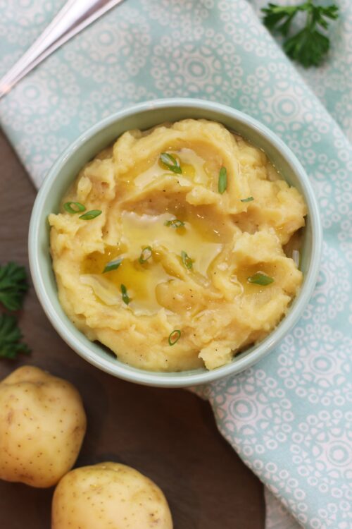 A bowl of mashed potatoes garnished with green onions and a drizzle of olive oil