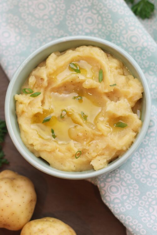 A bowl of mashed potatoes garnished with green onions and a drizzle of olive oil