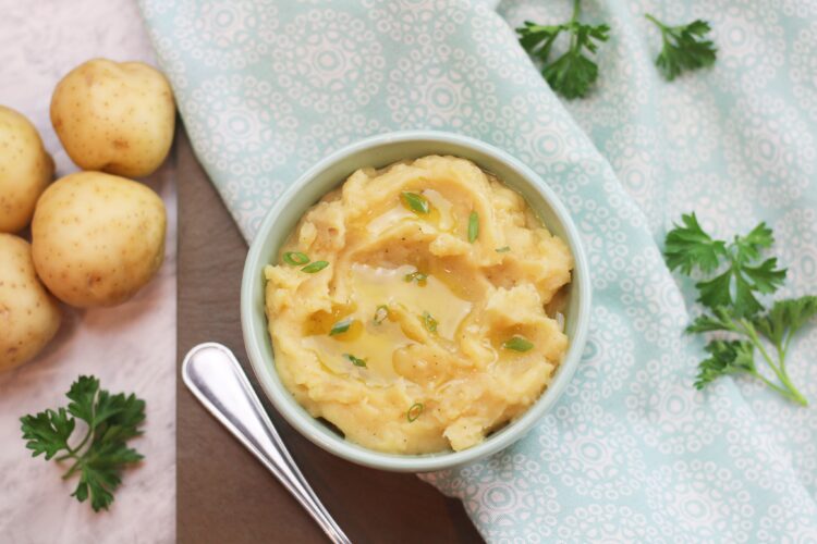 A bowl of mashed potatoes garnished with green onions and a drizzle of olive oil