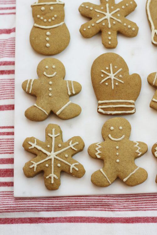 Gingerbread cookies with white icing on a white cutting board with a red and white striped background